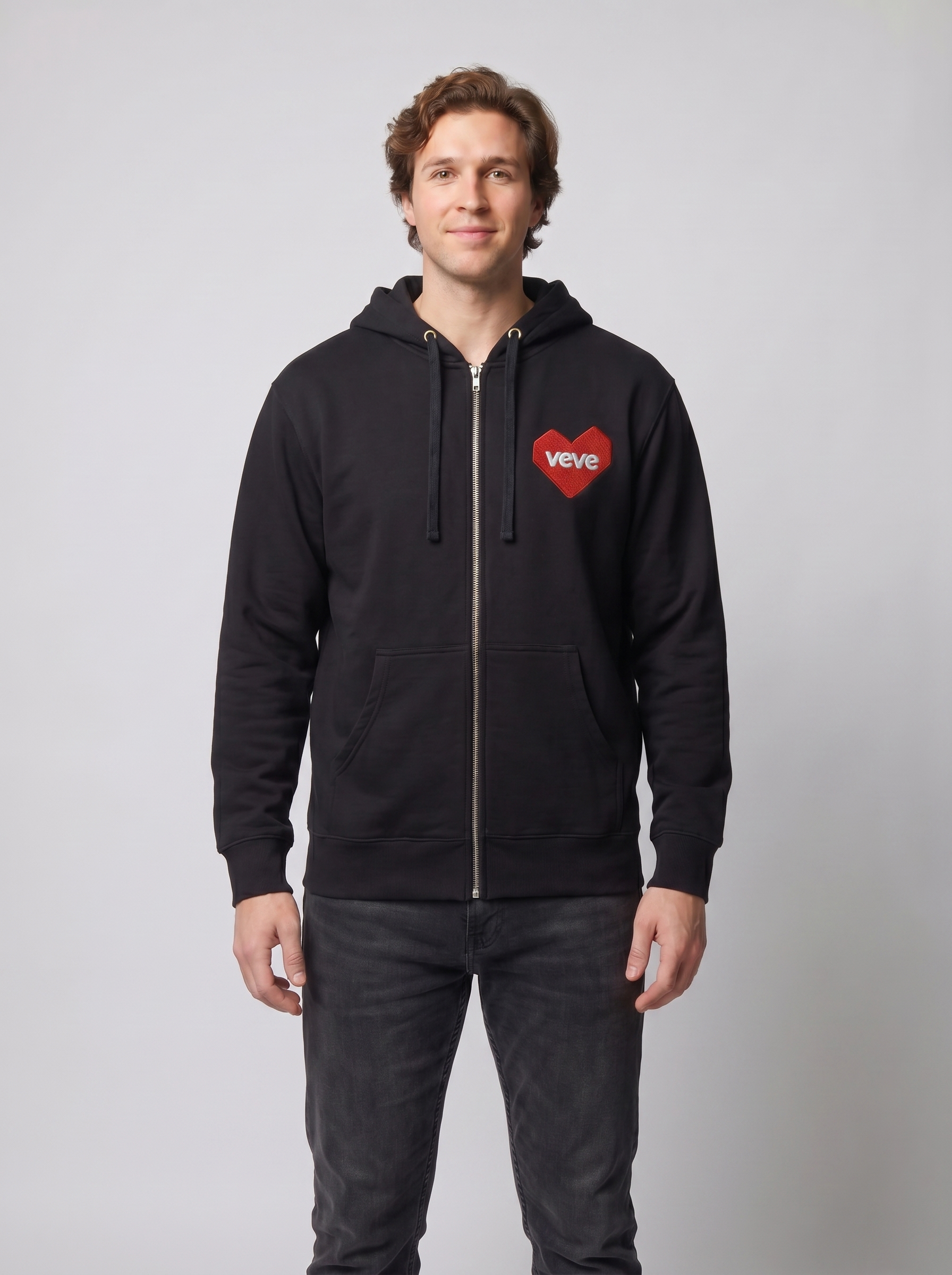Common Club VeVe Collectors at Heart Zip Up Hoodie — on-model studio fit photo, lean-build man wearing black Independent Trading Co. SS4500Z full-zip hoodie with red VeVe heart chest patch, front view showing relaxed midweight drape, zipped to throat, hood down